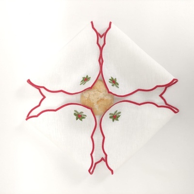 Guardanapo branco com bordas vermelhas e bordados florais a envolver pão