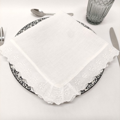 Guardanapo branco bordado sobre prato com padrão preto e branco, talheres e copo transparente