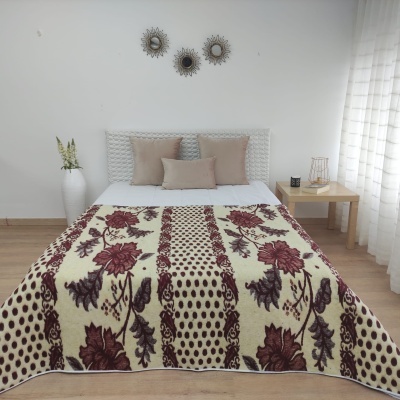 Cobertor floral castanho bege sobre cama branca com almofadas bege e mesa de madeira clara