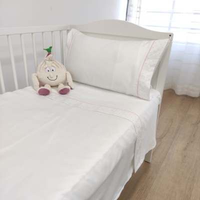 Cama branca de bebé com lençóis brancos e uma almofada de pelúcia em forma de alho