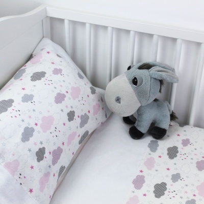 Cama de bebé com almofada e edredão com nuvens e estrela, e peluche de burro cinzento