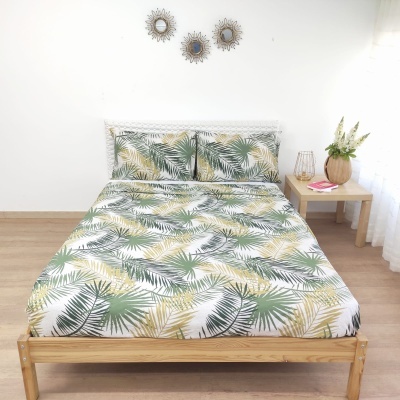 Cama de madeira com roupa de cama estampada de folhas verdes e amarelas num quarto com decoração simples e mesa de cabeceira clara