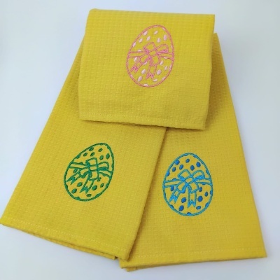 Três panos de cozinha amarelos com bordados de ovo da Páscoa coloridos