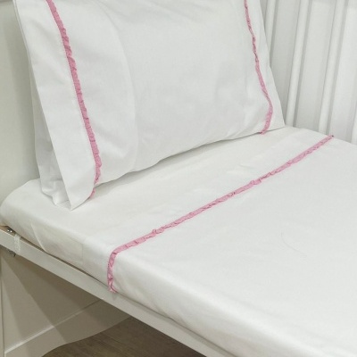 Conjunto de roupa de cama branca com bordado rosa em berço branco.