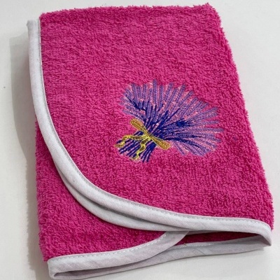 Toalha rosa felpuda com bordado de flor azul e amarelo e bainha branca em superfície branca