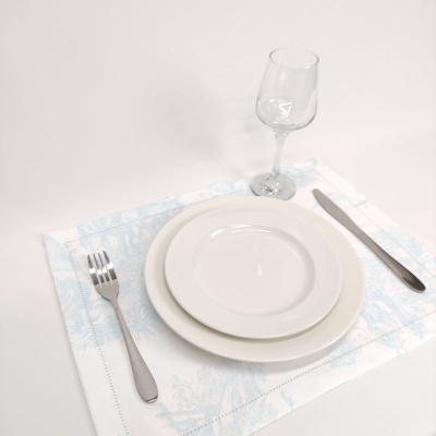 Conjunto de loiça branco com talheres metálicos e copo de vidro sobre jogo americano azul claro