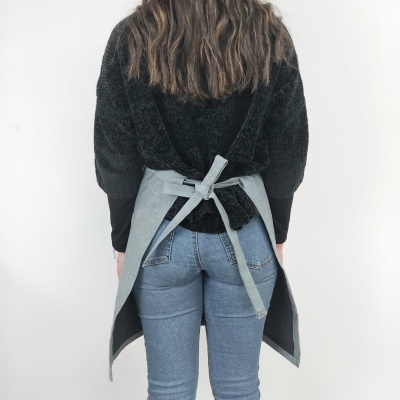 Pessoa de costas com camisola preta, calças de ganga azul e avental cinzento amarrado na cintura