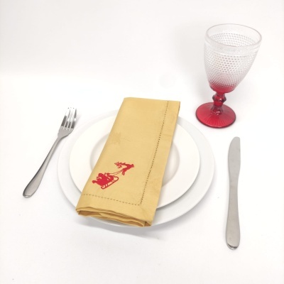 Conjunto de mesa com prato branco, talheres em metal, copo transparente com base vermelha e guardanapo amarelo bordado.