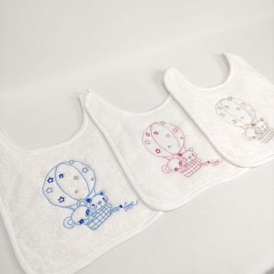 Três babetes brancos com bordados de balões e ursos em azul, rosa e bege