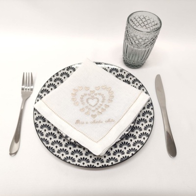 Mesa posta com prato padrão preto e branco, talheres, copo de vidro e guardanapo branco bordado