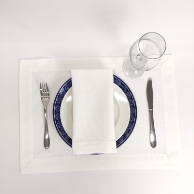 Conjunto de jantar com prato branco e azul, talheres prateados, guardanapo branco, copo de vidro e toalha branca