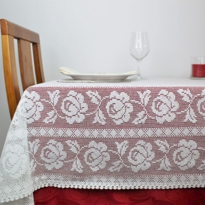 Mesa com toalha branca rendada com padrão floral, utensílios de mesa e cadeira de madeira