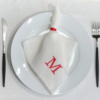 Guardanapo branco com letra M em prato branco e talheres com cabo preto