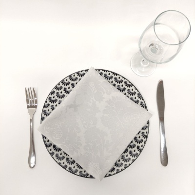 Conjunto de mesa com prato decorado, guardanapo branco, talheres em aço e copo de vidro.