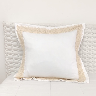 Almofada branca com bordado rendado bege sobre cama e colcha branca acolchoada