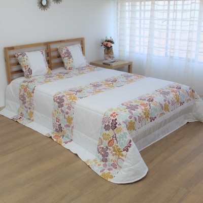 Cama com edredão branco e padrão floral em quarto com cabeceira e mesa de cabeceira