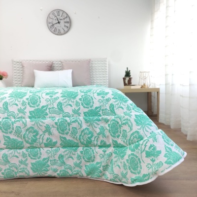 Edredão branco com padrão floral verde-água numa cama com cabeceira almofadada em quarto iluminado