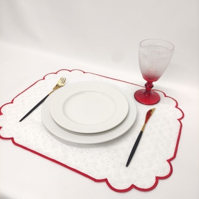 Lugar americano branco com borda vermelha, loiça branca, talheres pretos e dourados, e copo com haste vermelha.