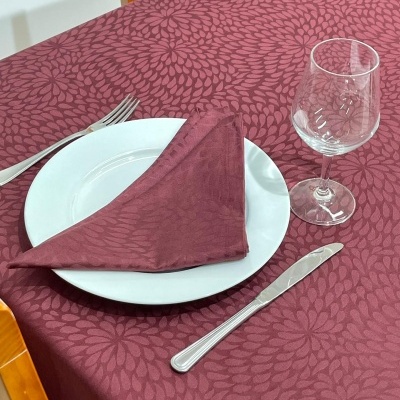 Mesa posta com toalha vinheta floral, prato branco, guardanapo vinho, talheres e taça de vidro