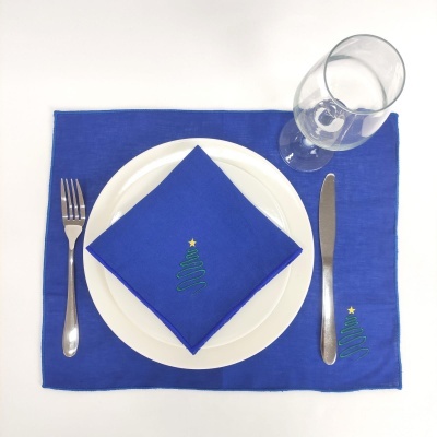 Jogo americano e guardanapo azuis com árvore de Natal, prato branco, talheres de metal e copo de vidro