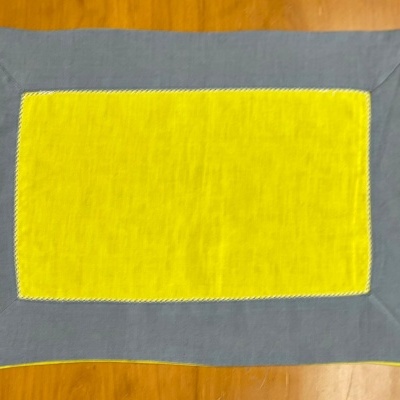 Toalha retangular cinza com centro amarelo sobre madeira clara