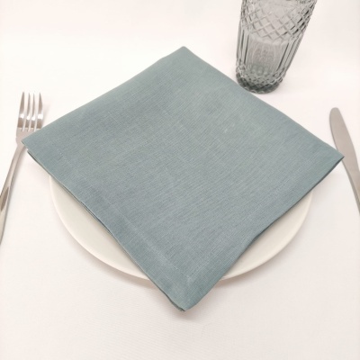 Guardanapo azul claro sobre prato branco, com talheres e copo ao lado