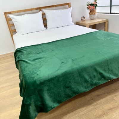 Cama com manta verde escura de tecido macio, almofadas e lençol brancos, e mesa lateral com vaso de flores