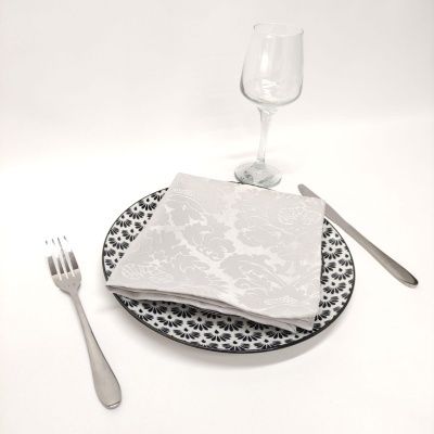 Conjunto de mesa com prato decorado, guardanapo branco, talheres metálicos e copo de vidro