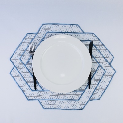 Conjunto de individuais hexagonais azul e branco com padrão de folhas com prato branco, garfo e faca