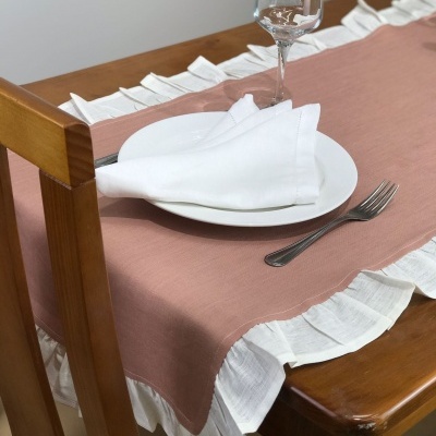 Passadeira de mesa rosa com bordas brancas plissadas sobre mesa de madeira com prato, guardanapo, garfo e taça