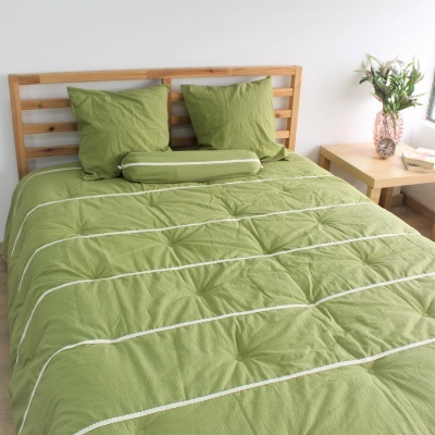 Cama com edredão verde e almofadas num quarto com mesa de cabeceira e jarro de flores