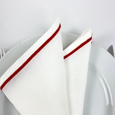Guardanapo branco com linha vermelha dobrado sobre prato branco e talheres ao lado.