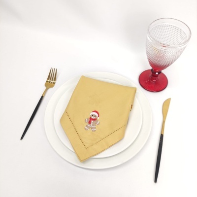 Mesa posta com pratos brancos, guardanapo amarelo bordado e talheres com cabos pretos e dourados, copo transparente com base vermelha