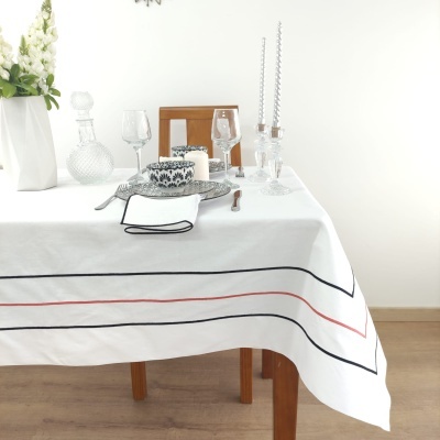 Toalha de mesa branca com linhas pretas e vermelhas sobre mesa de madeira com acessórios de jantar.