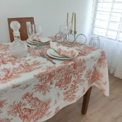 Toalha de mesa branca com padrão vermelho em mesa de madeira com pratos, copos, jarro de vidro e castiçais dourados