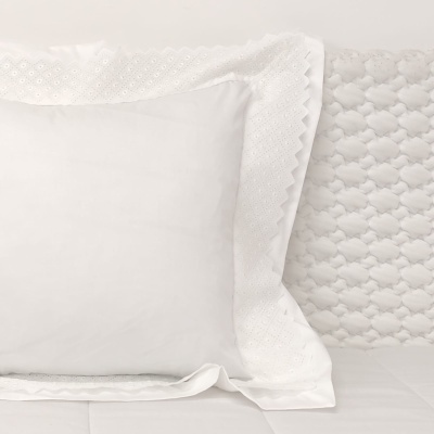 Almofada branca com capa bordada sobre cama com colcha acolchoada branca