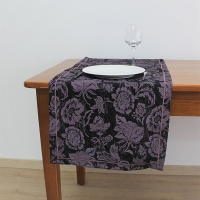 Toalha de mesa preta com padrão floral violeta sobre mesa de madeira com prato branco e copo de vidro.