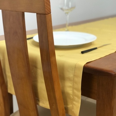 Cadeira de madeira com assento creme junto a mesa com toalha amarela, prato branco e taça de vinho.