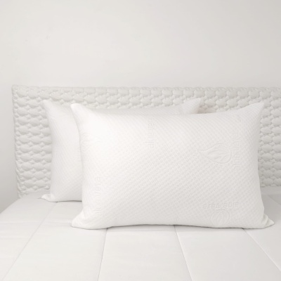 Duas almofadas brancas texturizadas em cama branca com cabeceira estofada.