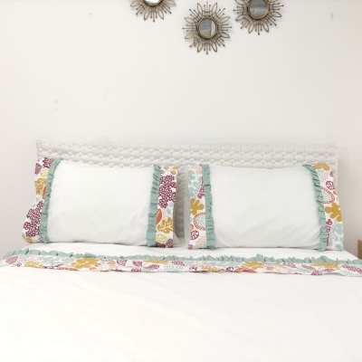 Cabeceira de cama branca com almofadas e tira decorativa floral colorida com pequenos espelhos na parede