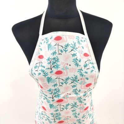 Avental branco com flamingos rosa e folhas verdes num manequim preto