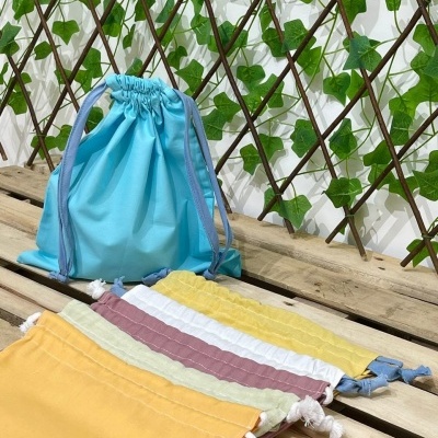 Sacos de tecido coloridos com fecho de cordão sobre madeira e parede com treliça e folhas verdes