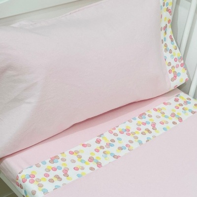 Jogo de cama cor-de-rosa com padrão de confetes coloridos em berço branco