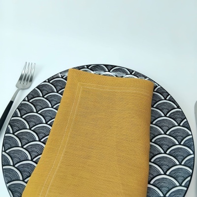 Prato com padrão preto e branco de ondas, guardanapo amarelo e garfo numa mesa branca
