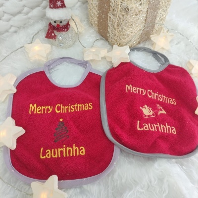Dois babetes vermelhos bordados com nome Laurinha e decoração de Natal, luzes em forma de estrela e boneco de neve pequeno ao fundo