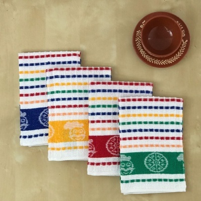 Quatro panos de cozinha coloridos com linhas e símbolos circulares ao lado de um prato castanho