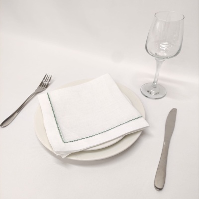 talheres aço inox, prato branco, guardanapo branco com borda verde, copo de vinho transparente