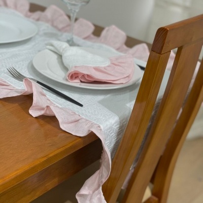 Toalha de mesa branca com borda rosa em mesa de madeira com prato e copo