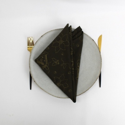 Conjunto de mesa minimalista com prato cinza, guardanapo castanho com padrão dourado, talheres dourados e pretos.