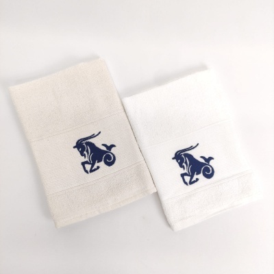 Dois toalhetes com bordado de bode azul, um bege e outro branco.